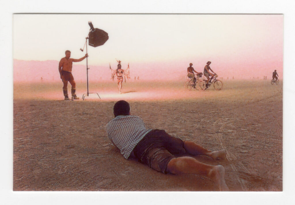 Behind-the-scenes of Allen Luke crawling on ground at Burning Man during a photoshoot outdoors