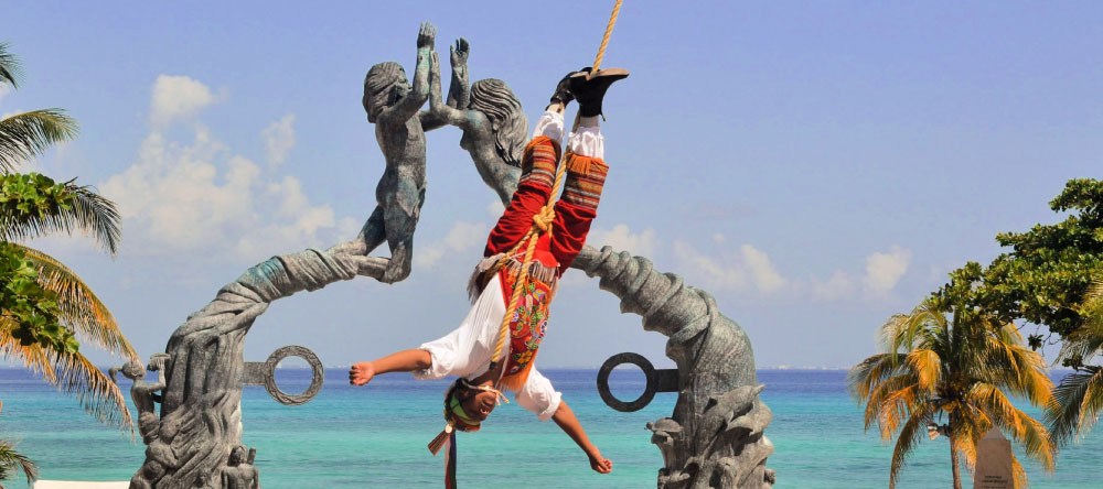 Landscape photo of a traditional Mayan cultural performance in front of the large city sculpture in Playa del Carmen